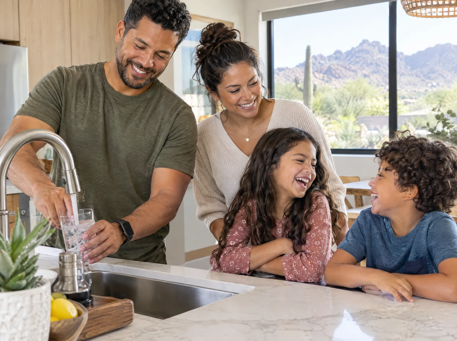 A family laughing at the kitchen sink while filling a glass of water