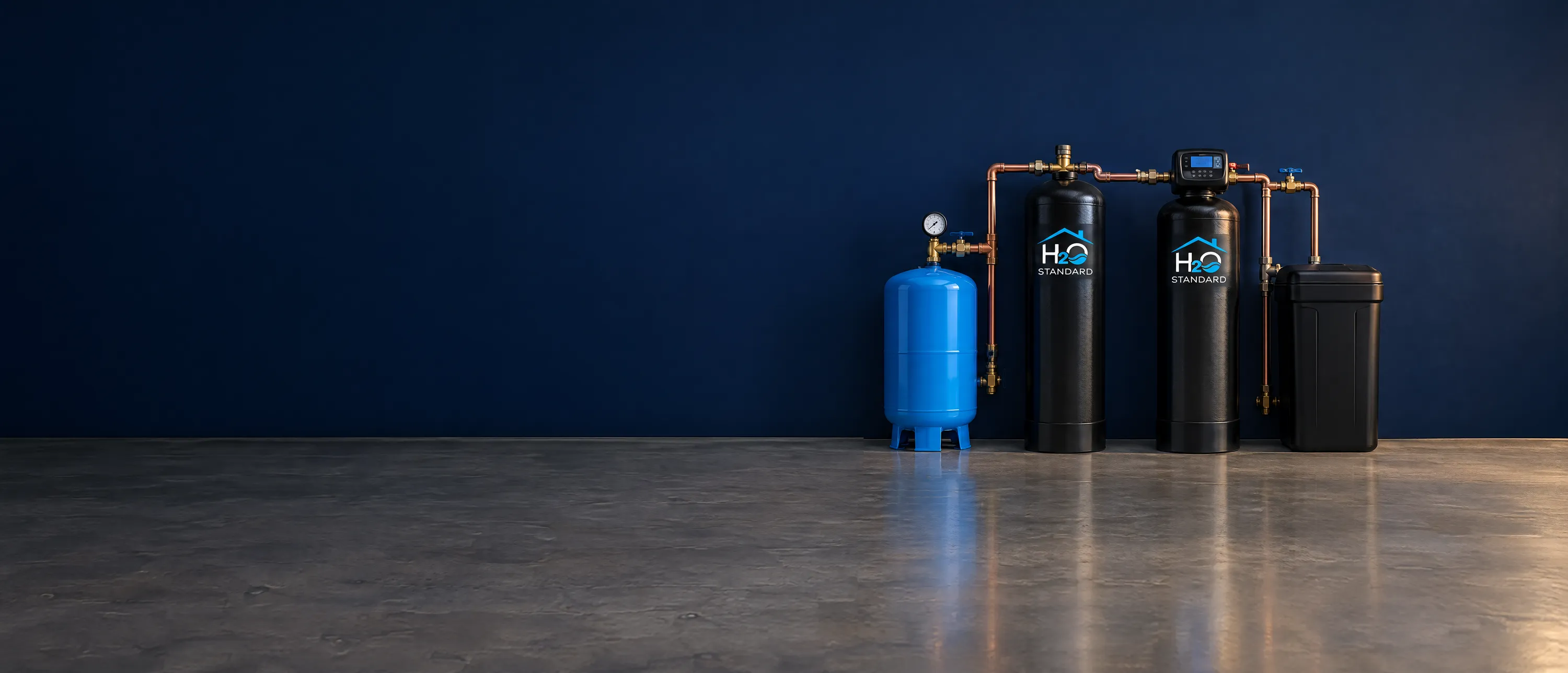 The H2O Standard well water system: a well pressure tank, an iron and sulfur filter, a softener and a brine tank against a navy wall