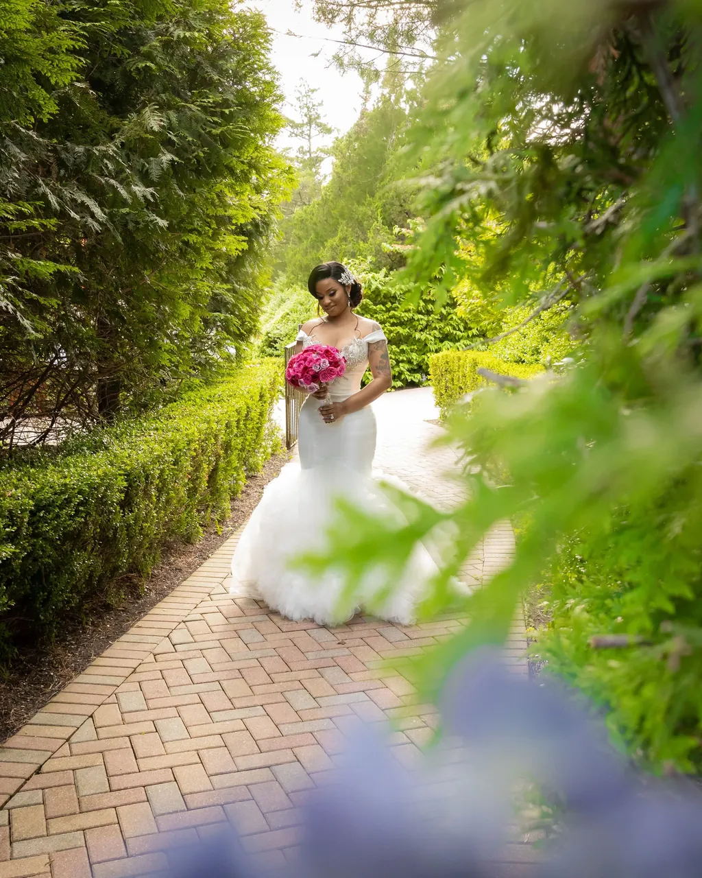 Bride in a white gown on a garden path framed by leaves