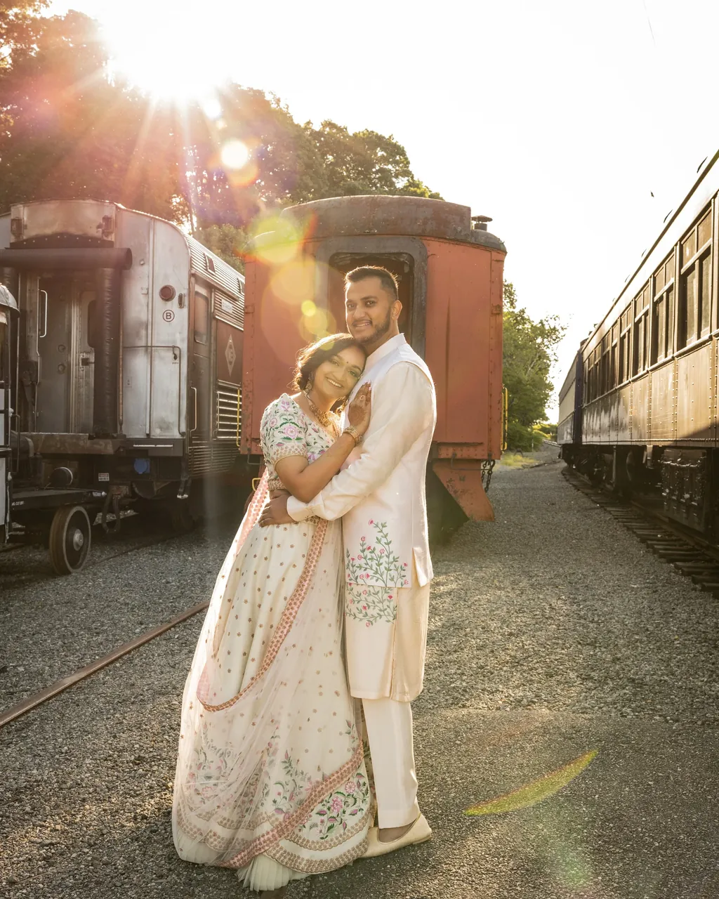 Bride and groom in ivory embracing beside a train at sunset