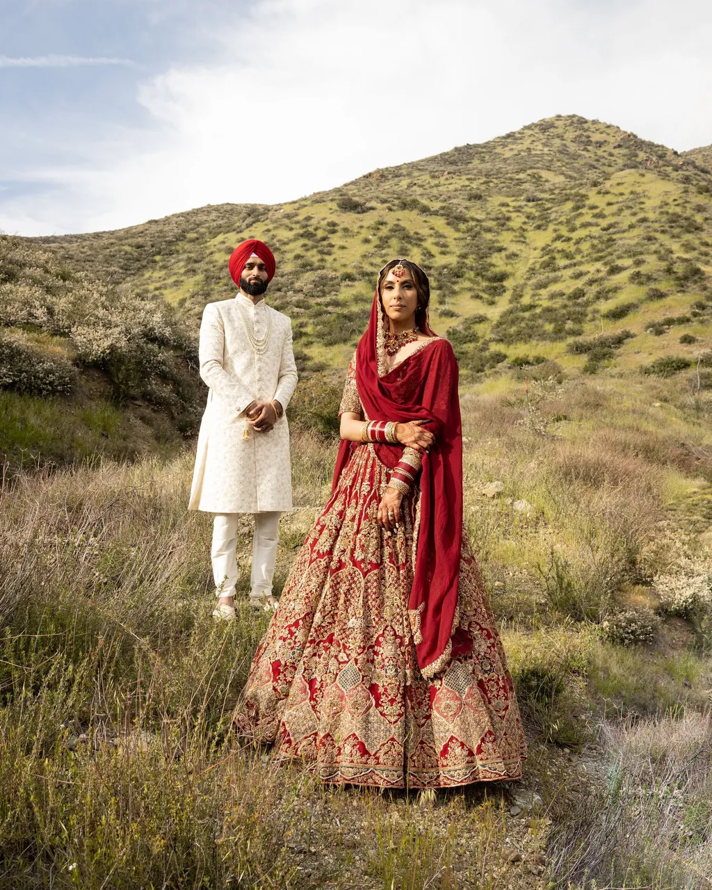 Sikh groom in a red turban and bride in a red lehenga in golden hills