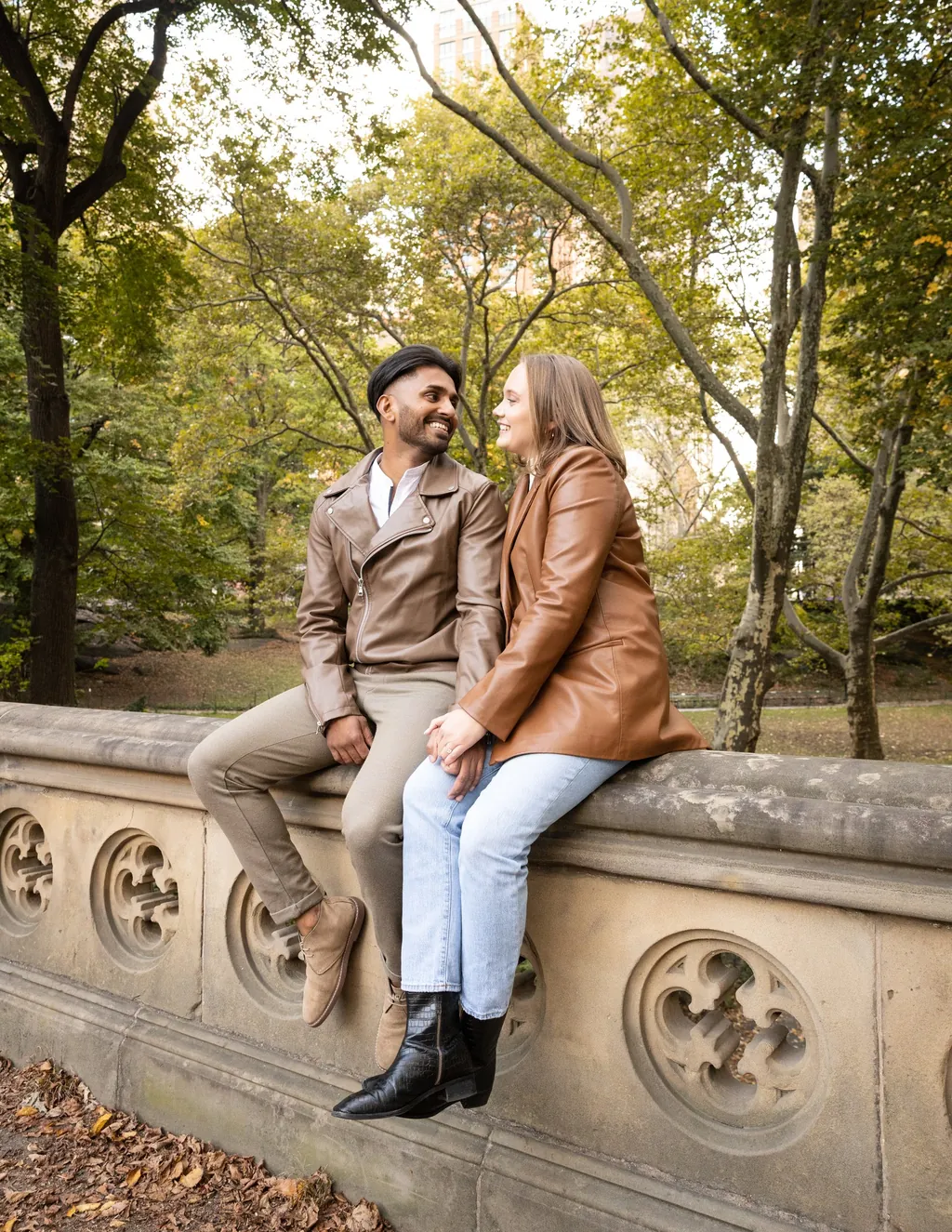 Engaged couple seated on a carved stone wall among autumn trees