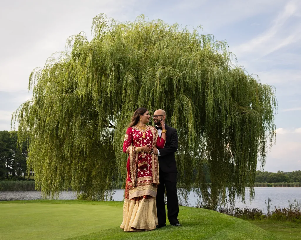Bride and groom under a willow tree by a lake