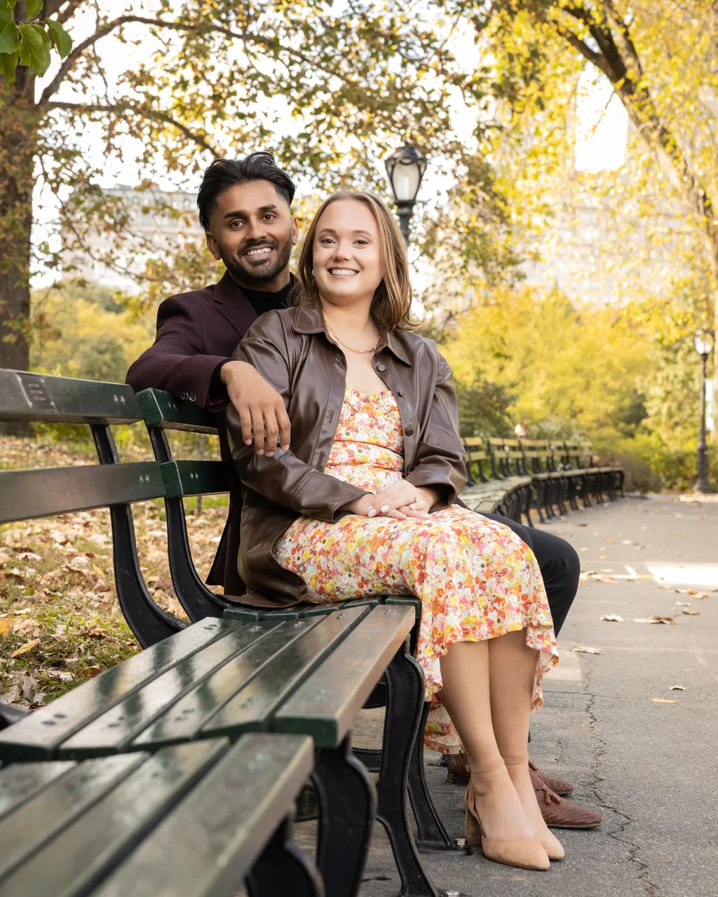 Engaged couple on a park bench beneath autumn trees