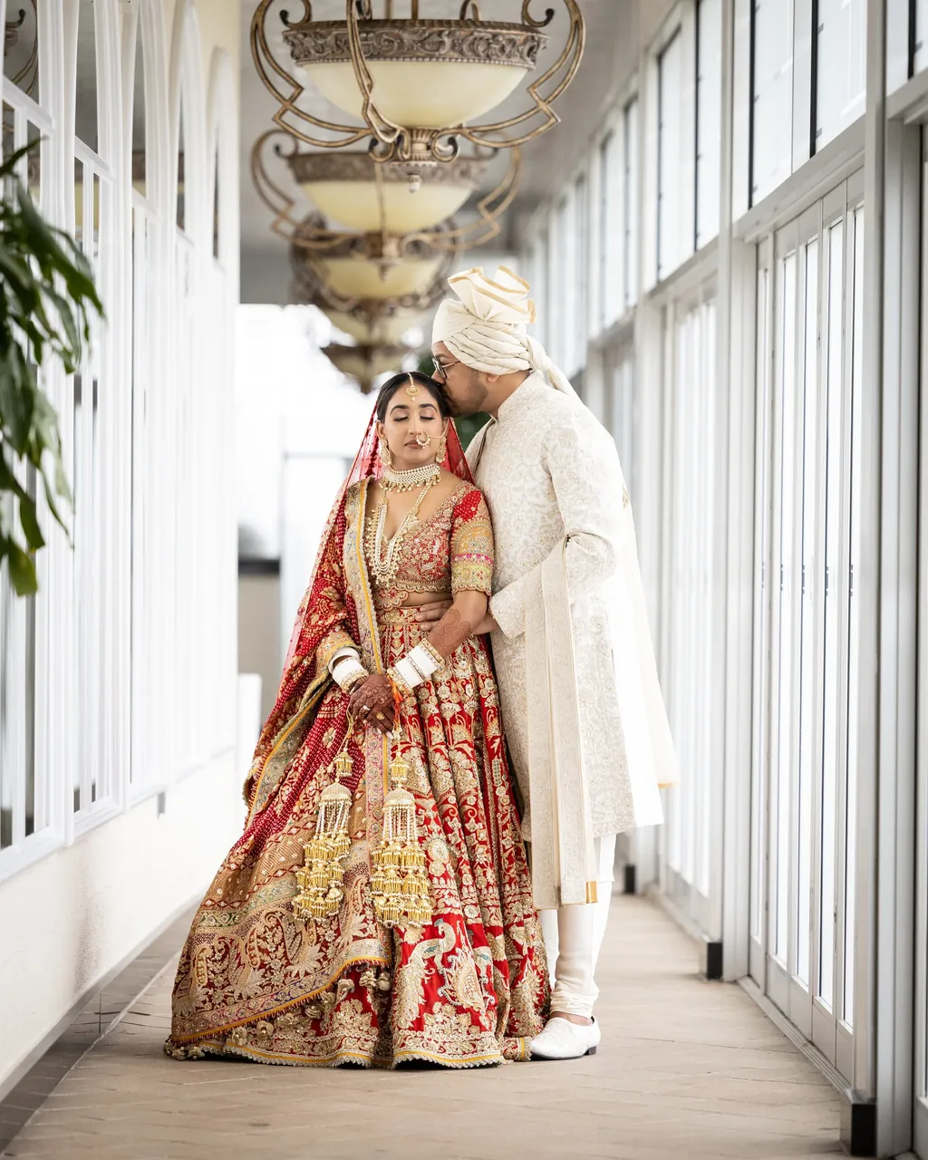 Bride and groom in red and gold on a sunlit glass porch