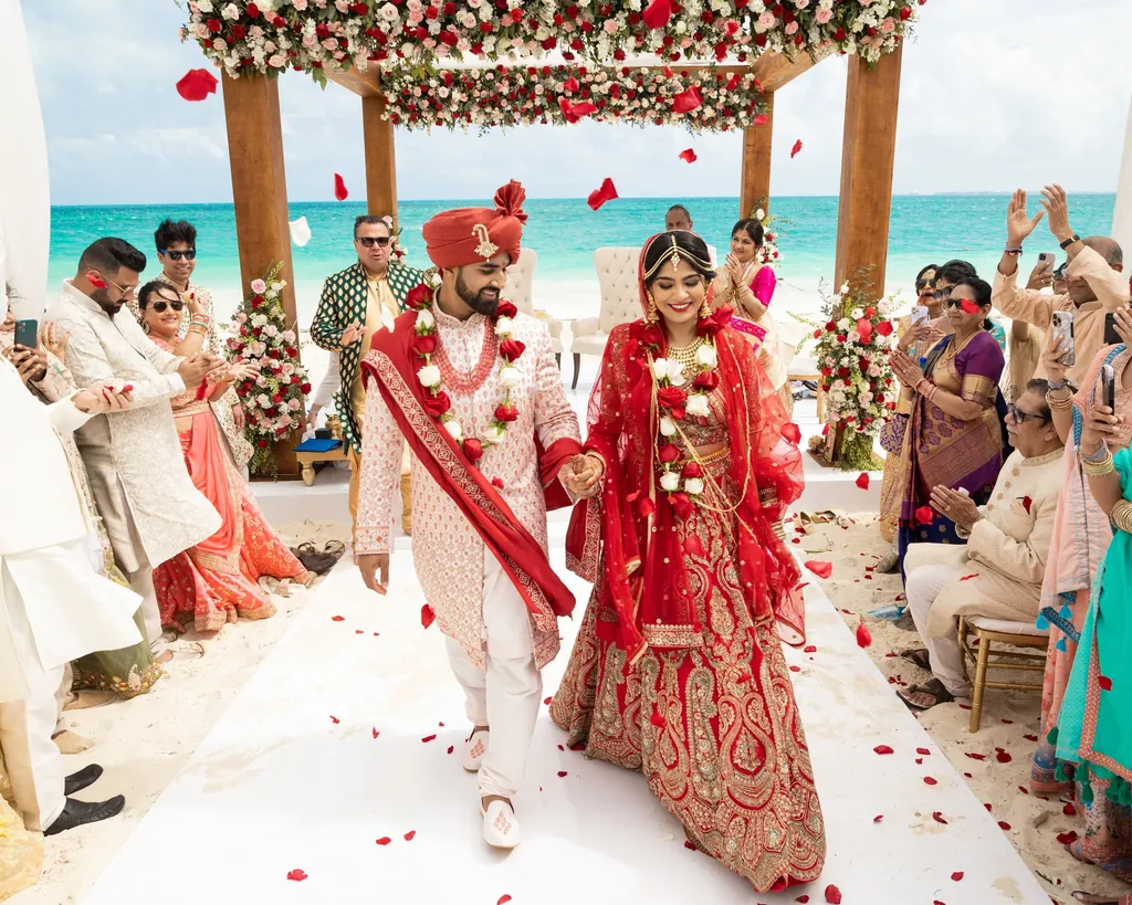Bride and groom walking out of a beach mandap through a shower of petals