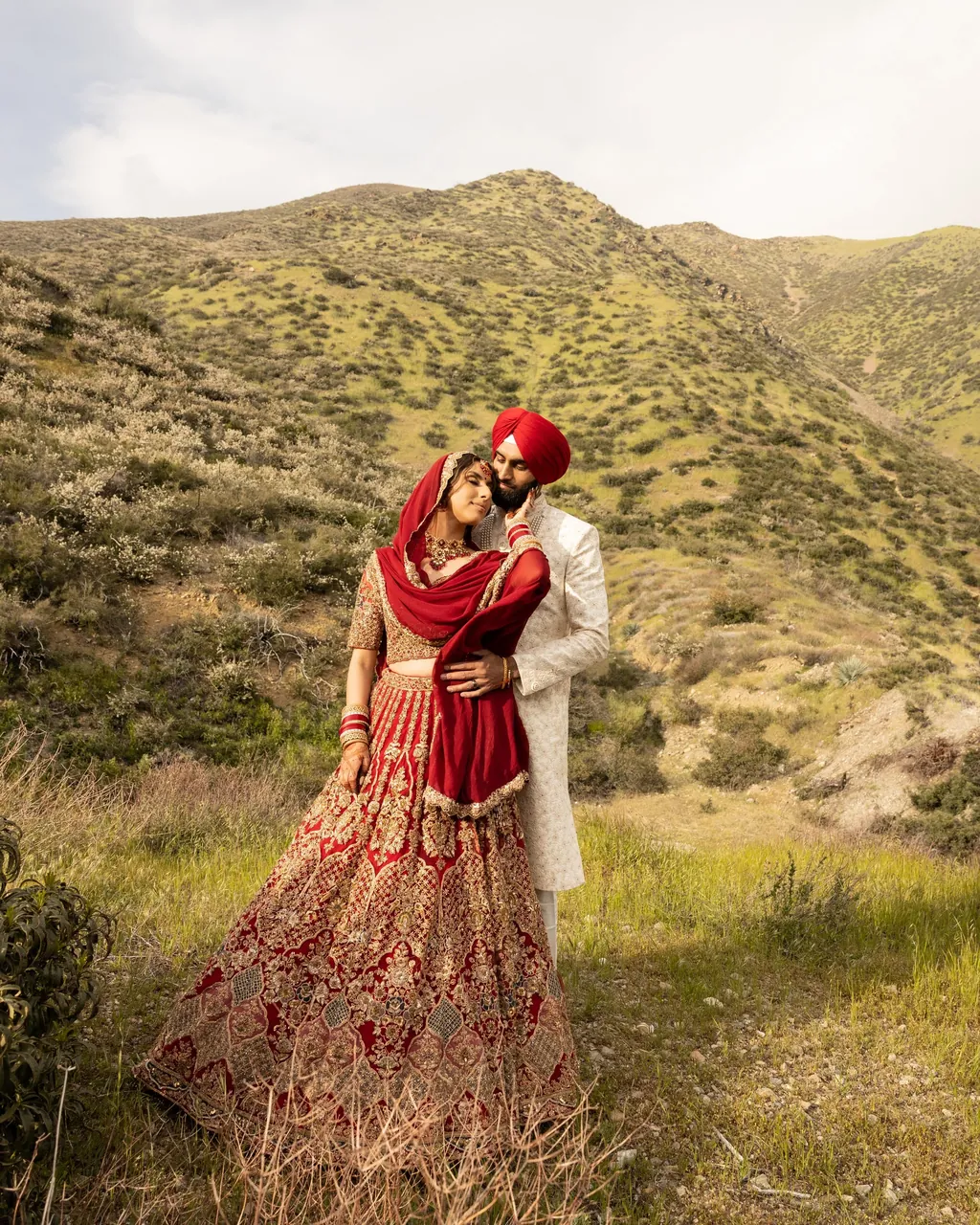 Bride in a red lehenga in tall grass on a hillside