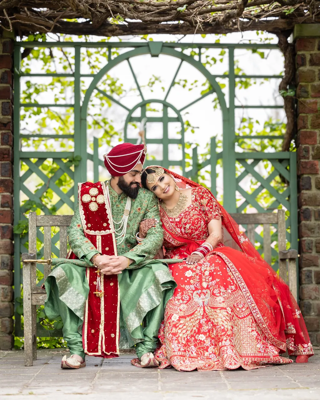 Sikh bride and groom in red and green laughing under a garden trellis