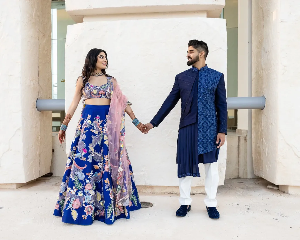 Couple holding hands, she in a royal blue lehenga, he in navy