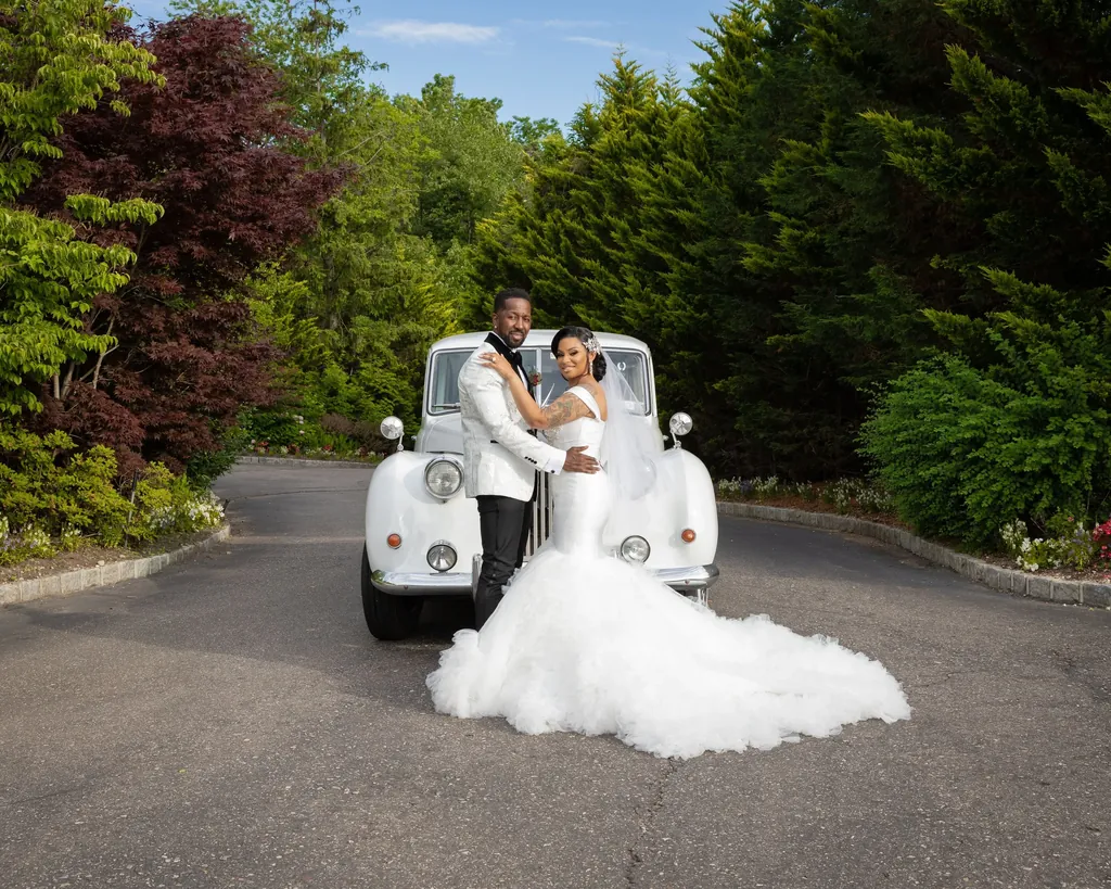 Bride in a white gown and groom beside a vintage car