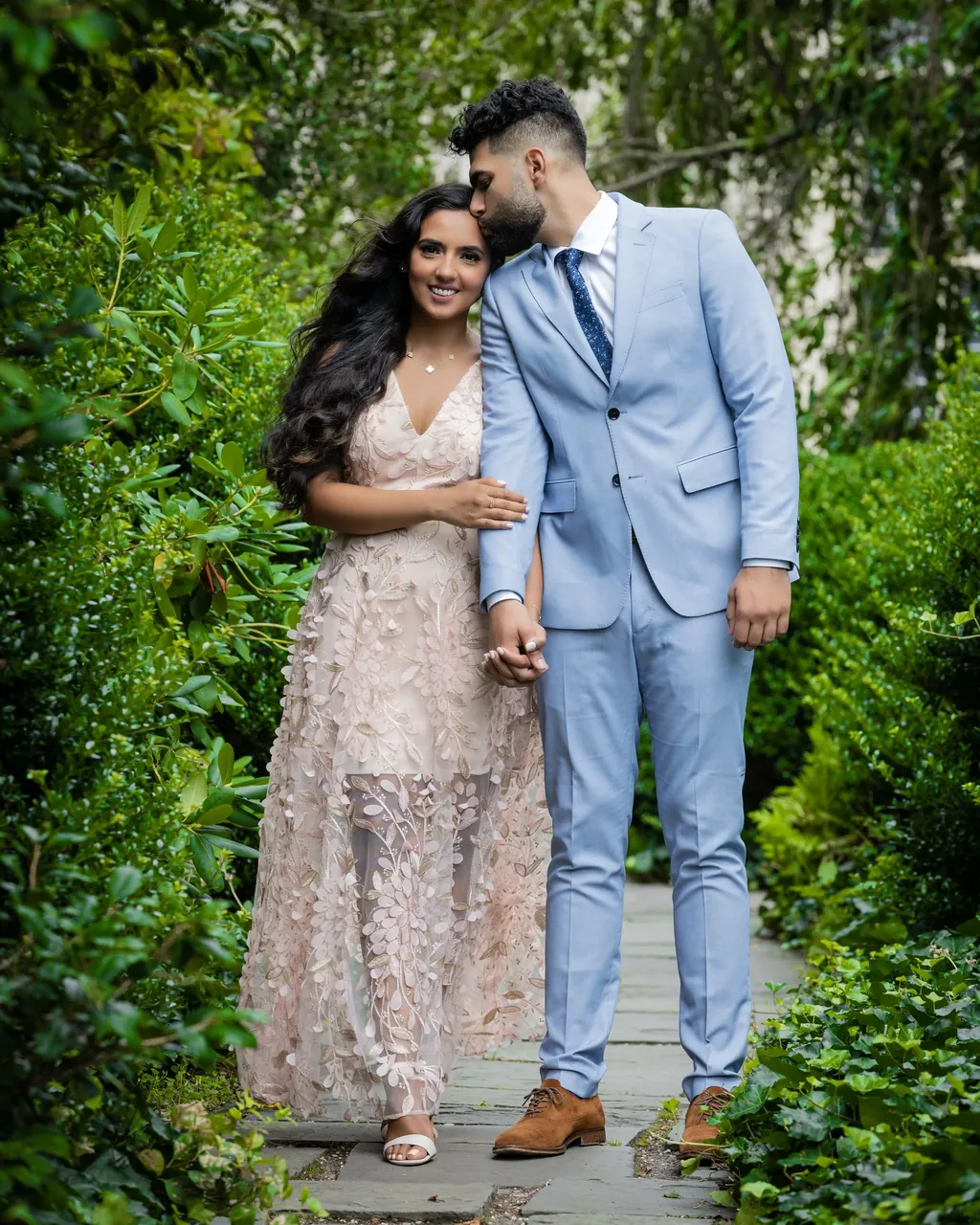 Engaged couple in a garden, she in a blush lehenga, he in a pale blue suit