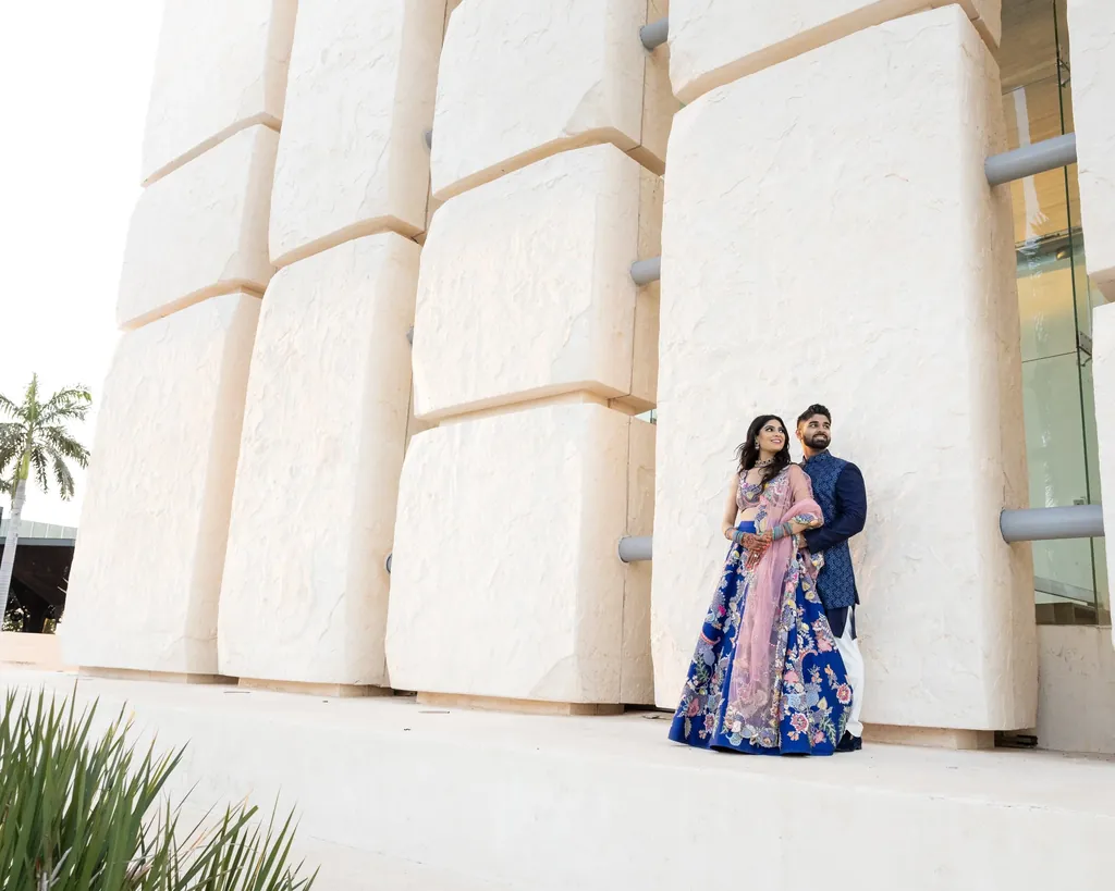 Couple in a blue lehenga and sherwani against a sculpted white wall