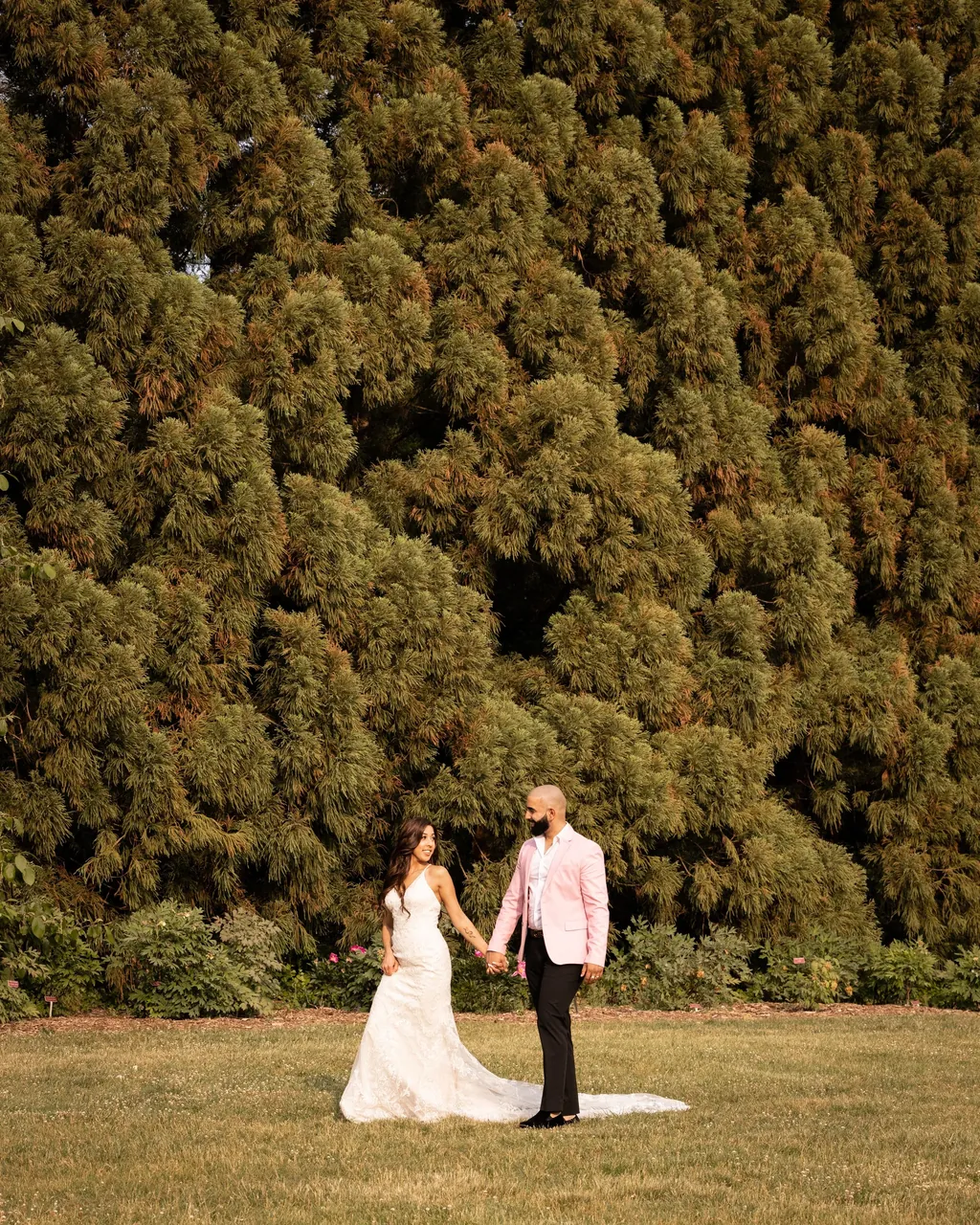 Bride and groom walking in front of a tall clipped hedge