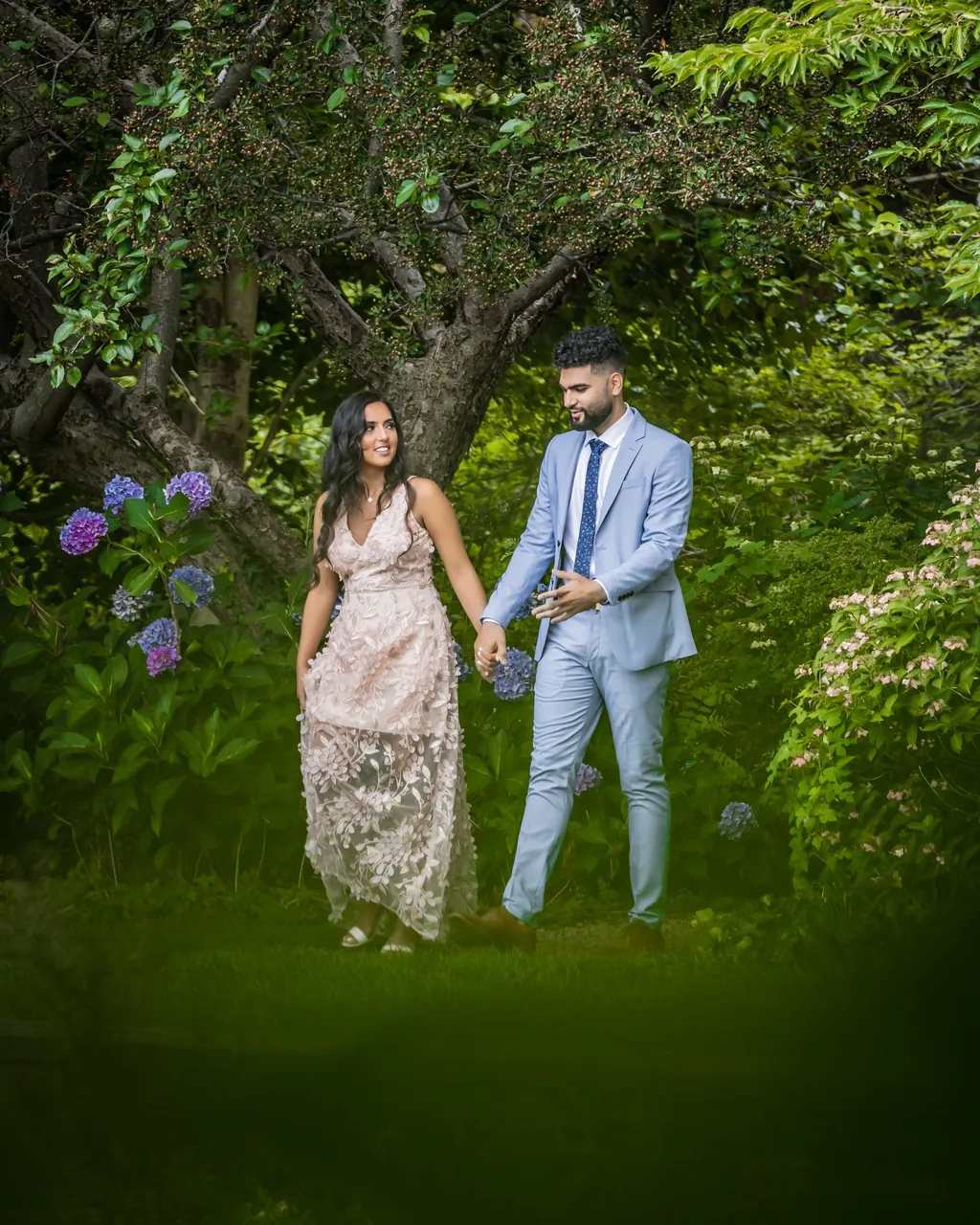 Couple walking hand in hand through a green garden