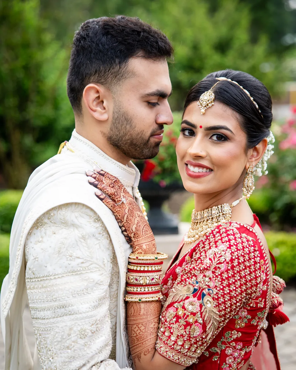 Groom in an ivory sherwani with his smiling bride in red and mehndi