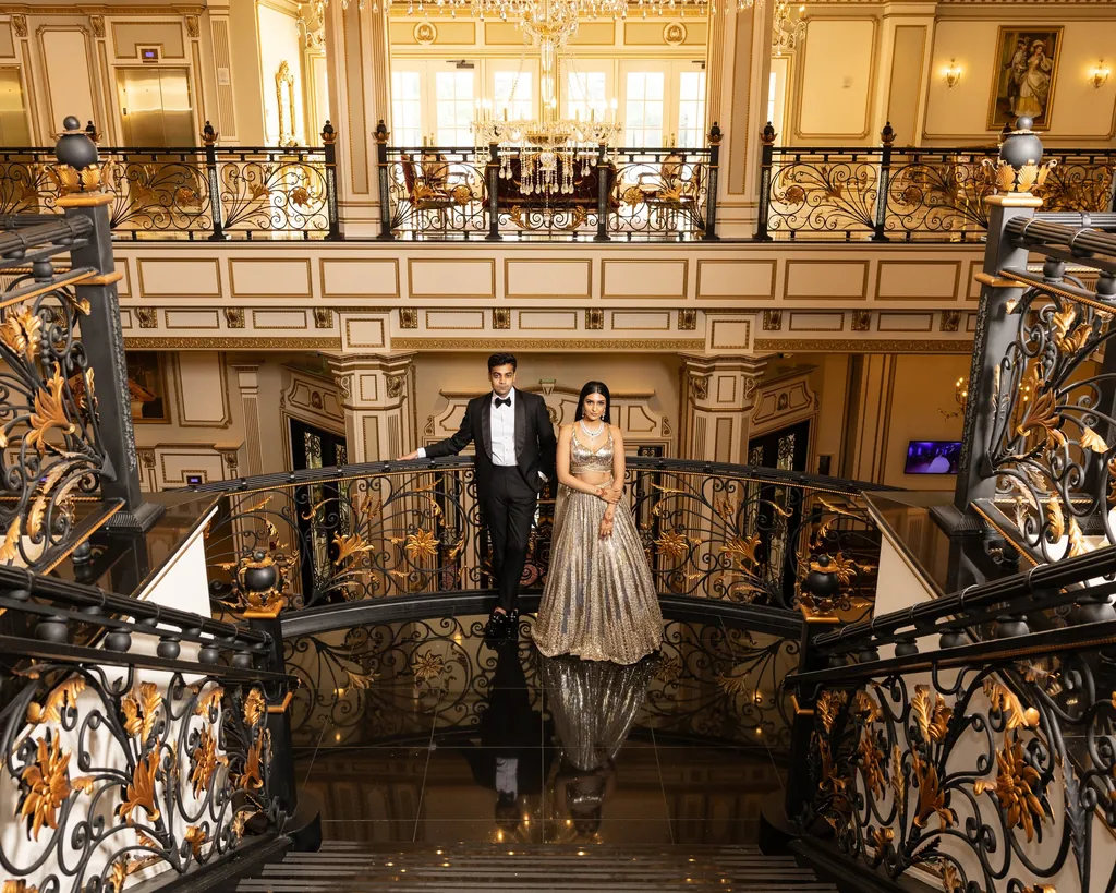 Bride in a silver lehenga and groom on a gilded wrought-iron staircase