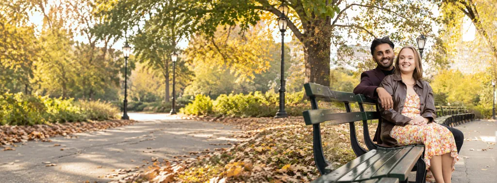 Engaged couple smiling on a park bench under autumn trees and iron lamp posts