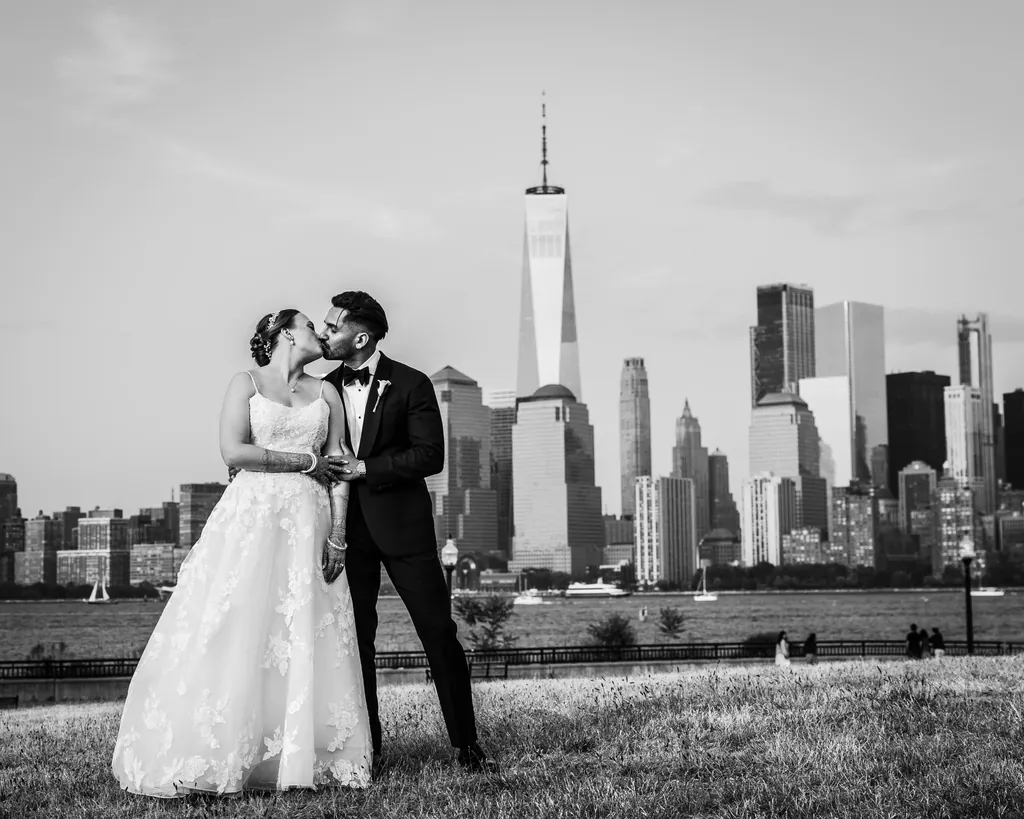 Black and white photo of a bride and groom kissing with the lower Manhattan skyline behind them