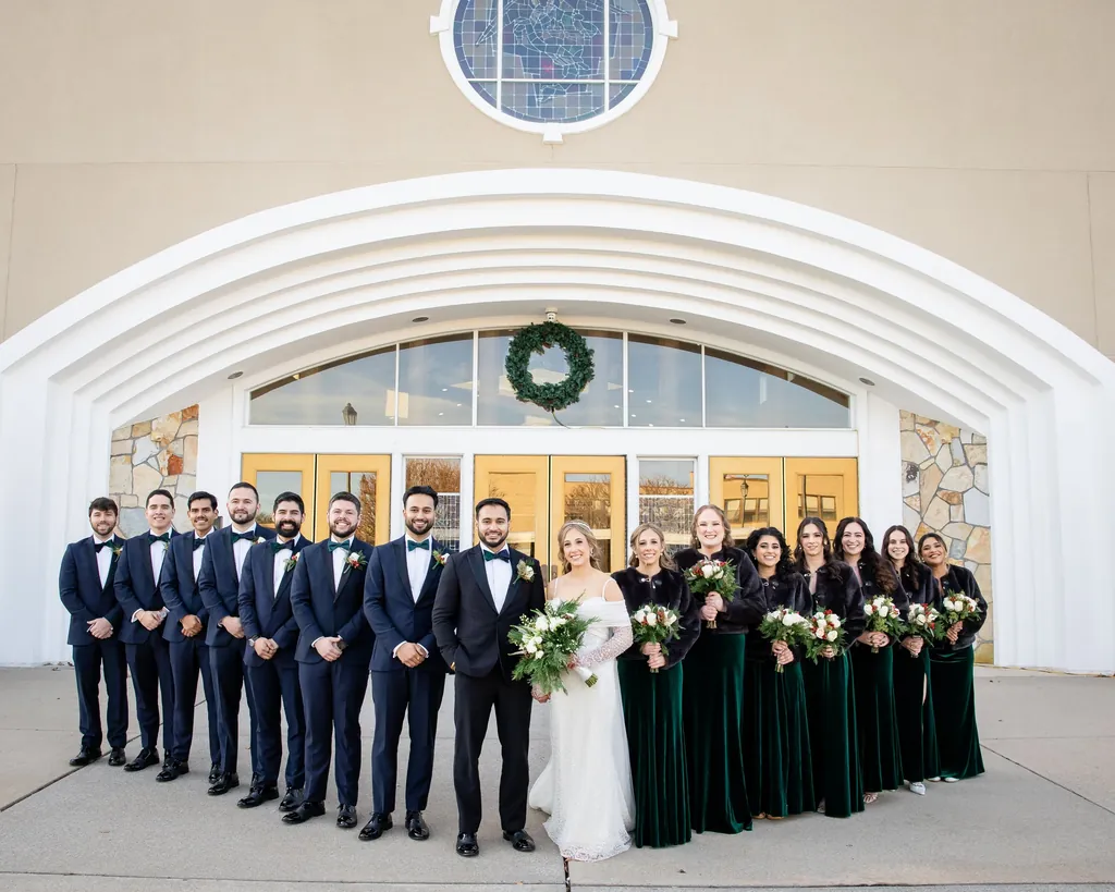 Wedding party in navy tuxedos and emerald gowns outside the venue entrance