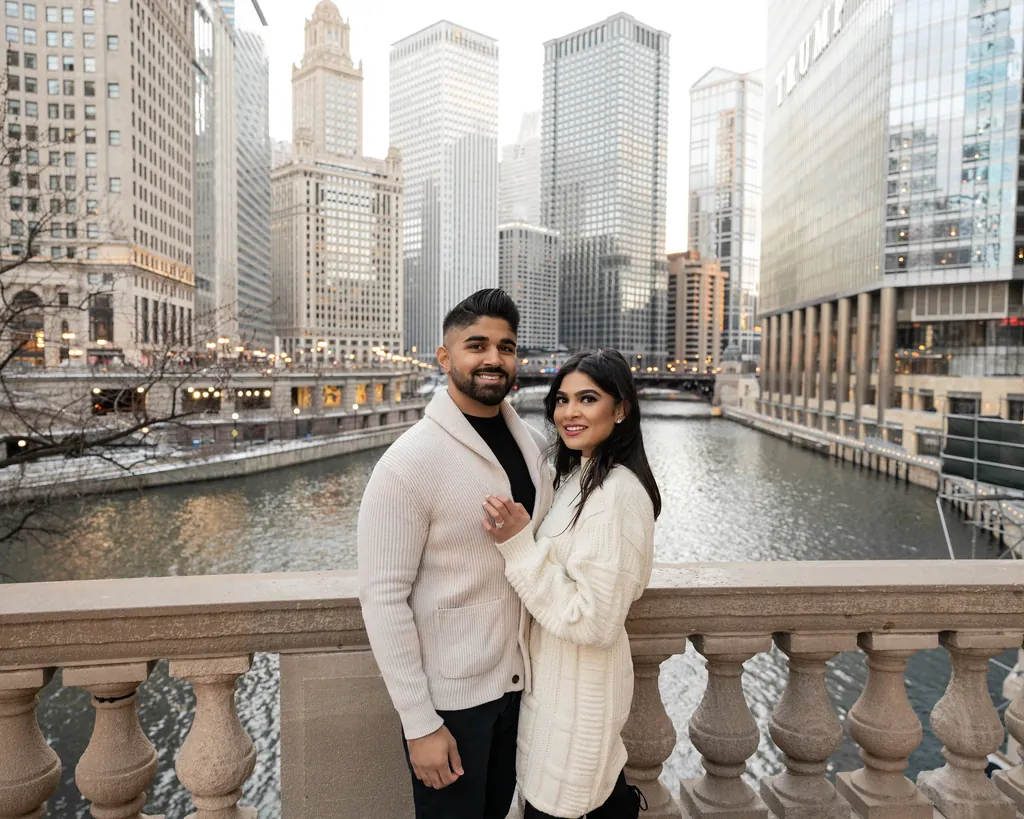 Couple in cream sweaters on a riverside balustrade among city towers