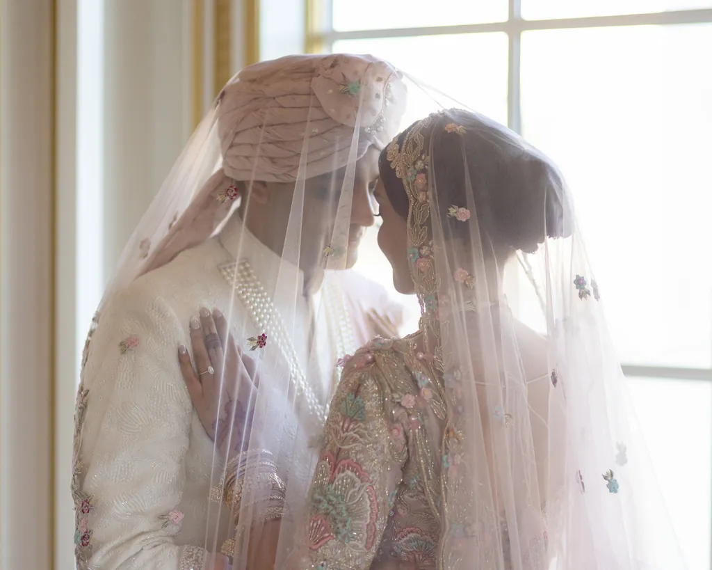 Bride and groom touching foreheads beneath a sheer embroidered veil